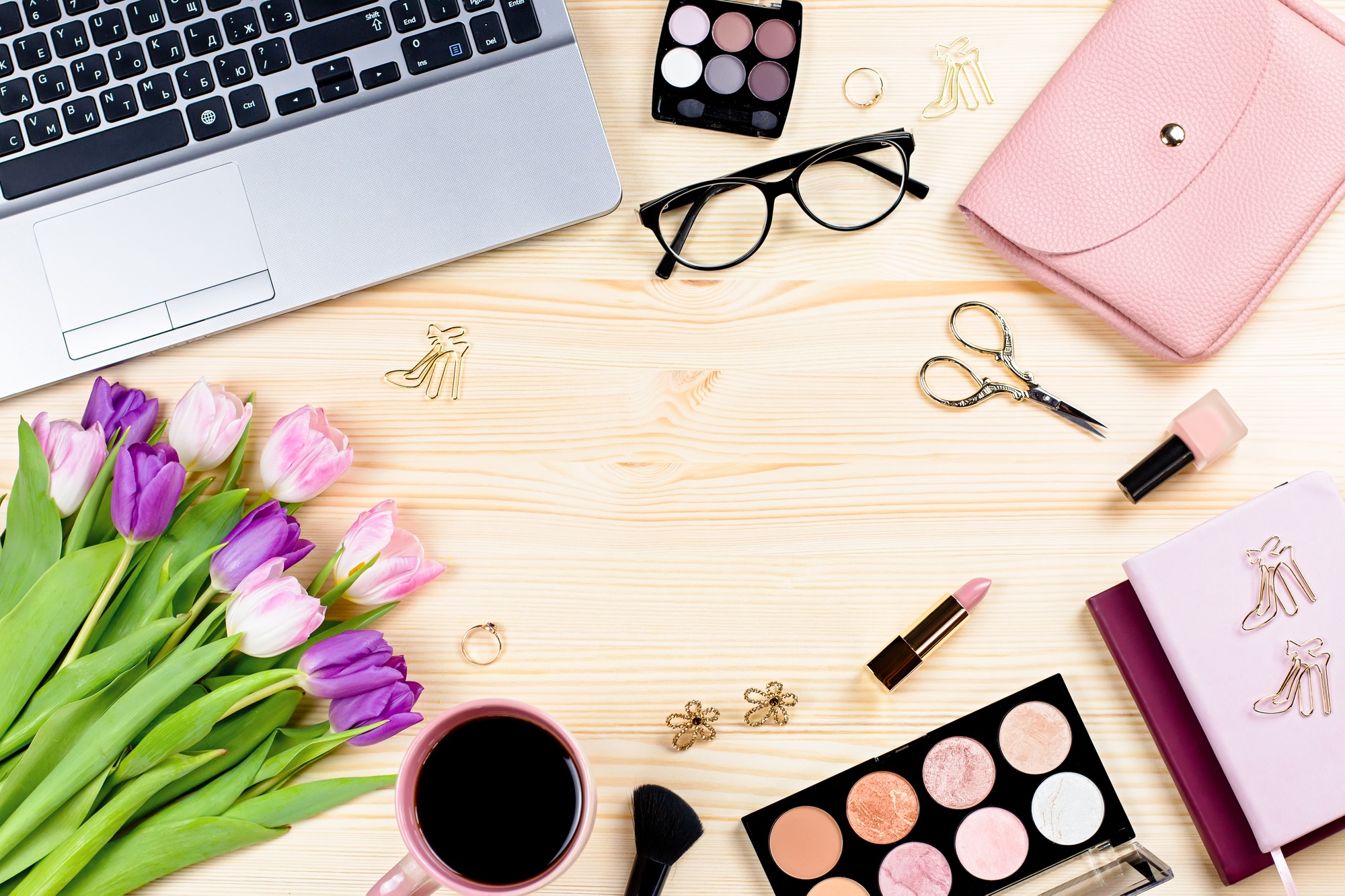 Woman office desk with notebooks, laptop, makeup products, bouquet, stationery